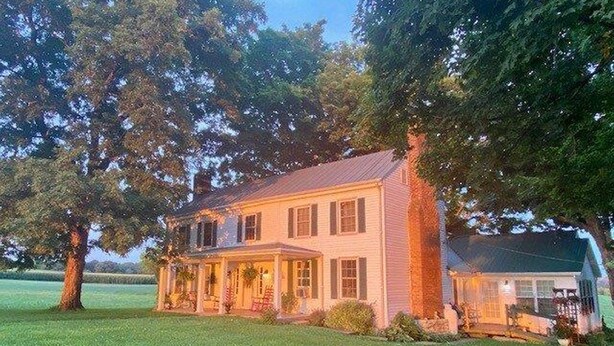 Une maison à deux étages avec un porche, entourée d’arbres et d’une pelouse bien entretenue.