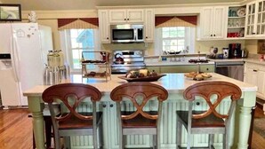 Une cuisine avec des meubles blancs, un îlot central doté de tabourets, un four à micro-ondes et une cuisinière.