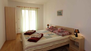 A bedroom with a bed, two bedside lamps, a small desk, a window with curtains, and a door. - Holiday apartment mit Klimaanlage (Šilo)