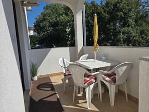 Un patio al aire libre con una mesa y sillas blancas, un paraguas amarillo y una planta en maceta.