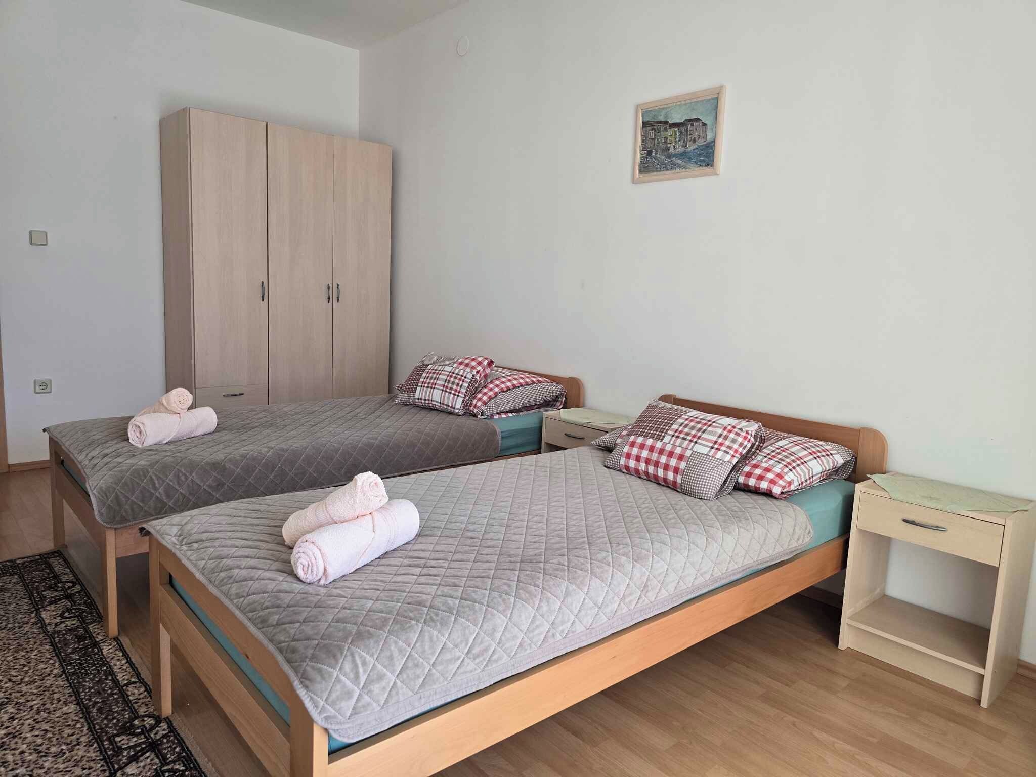 Une chambre avec deux lits, une armoire, un bureau et un petit tableau accroché au mur.