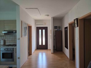 A narrow hallway with a kitchen on one side, a dark door at the end, and a refrigerator on the other side.