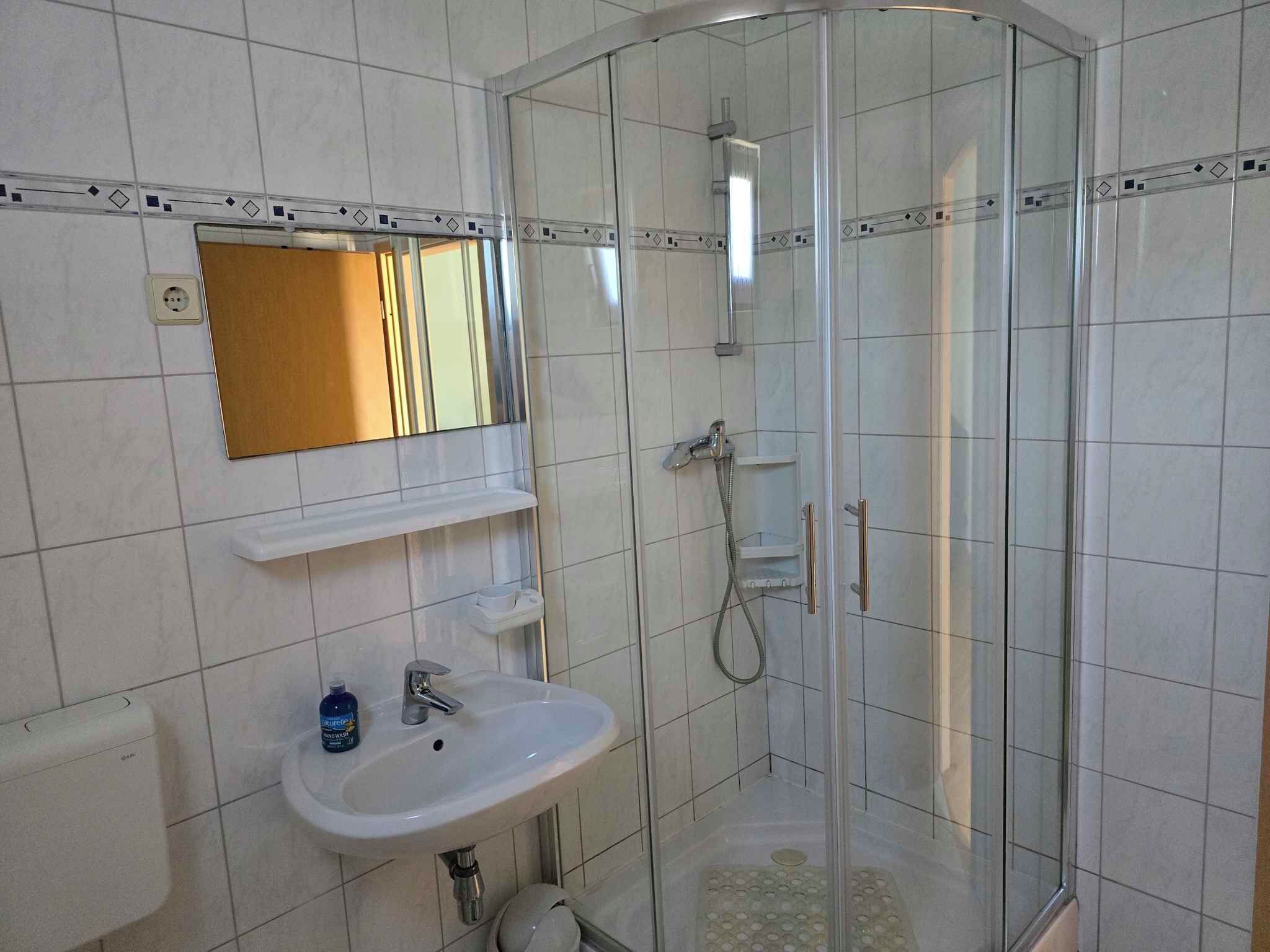 A modern bathroom with a glass shower enclosure, a sink with a mirror above it, and a hand soap dispenser.