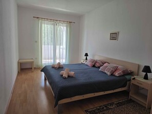 Un dormitorio con cama, mesitas de noche, una ventana con cortinas y un cuadro pequeño en la pared.