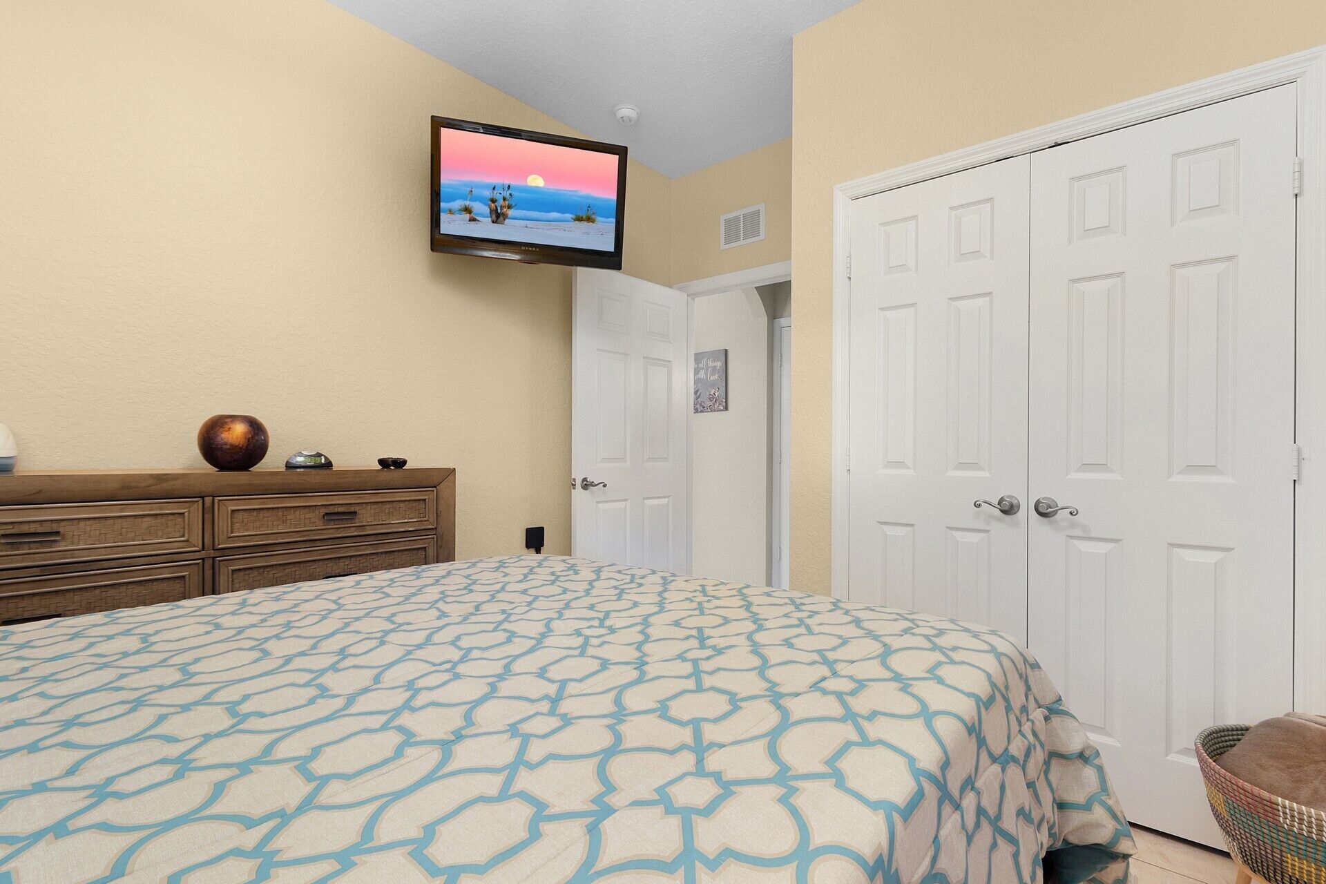 A bedroom with a bed, a dresser, a television mounted on the wall, and a set of double doors.