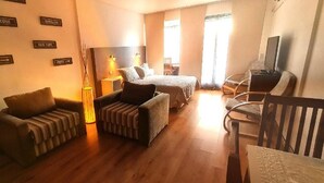 Un salon confortable avec un canapé, un fauteuil, un téléviseur et une lampe. Des panneaux sur le mur indiquent les directions vers différentes villes.