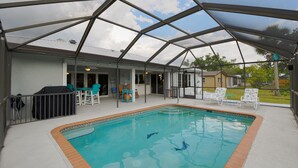 A covered outdoor swimming pool with a clear roof, surrounded by lounge chairs and a barbecue area. - Pool Home in Fort Meyers (Fort Myers)
