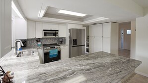 A modern kitchen with white cabinets, stainless steel appliances, and a granite countertop. - Pool Home in Fort Meyers (Fort Myers)