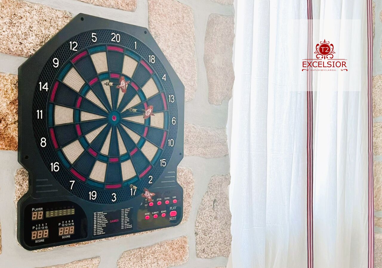 A dartboard mounted on a stone wall with a score display and buttons for play and next.