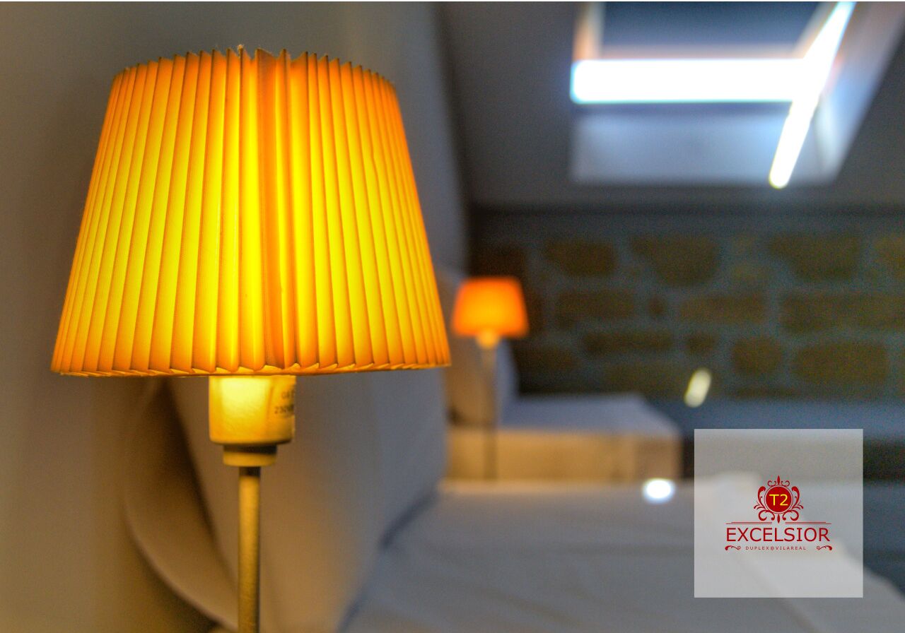 Quarto com luminária na parede e logotipo visível na parede.