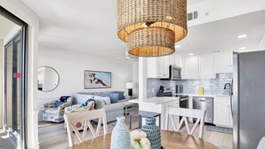 A modern kitchen with white cabinets, a stainless steel refrigerator, and a dining area with a wooden table and chairs.