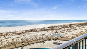 A beach view from a balcony with a pool, a sandy beach, and a clear blue sky.