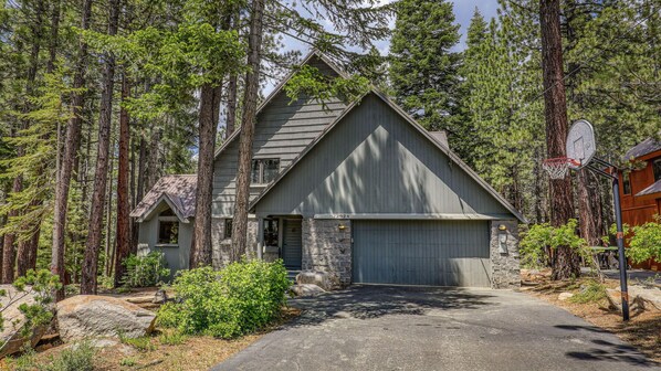A two-story house with a stone foundation, a garage, and a basketball hoop in the driveway. - Ponderosa Pine Escape (Truckee)