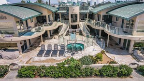 A modern hotel with a central pool, multiple balconies, and a glass-enclosed lounge area.