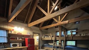 A cozy cabin interior with a sofa, wooden beams, a kitchen area, and a bunk bed. - Cherry Treesort "Trevor's Layaway" (China Grove)