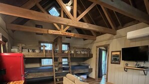 A rustic cabin interior with a loft bed, a sofa, a kitchen area, and a TV mounted on the wall. - Cherry Treesort "Trevor's Layaway" (China Grove)