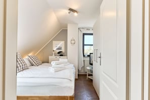Un dormitorio con una cama bien hecha, una mesita de noche con una lámpara y una ventana con cortinas.