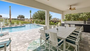 An outdoor pool area with a dining table and chairs, ceiling fans, and a view of the surrounding landscape. - Imagination at Reunion | 9 BR, Custom Built Theme Room, Game Room, Movie Theater (Kissimmee)