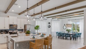 A modern kitchen with a central island, dining area with blue chairs, and a view of the outdoors. - Imagination at Reunion | 9 BR, Custom Built Theme Room, Game Room, Movie Theater (Kissimmee)