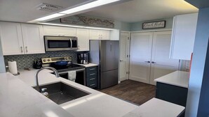A modern kitchen with white cabinets, stainless steel appliances, and a wooden floor. - Beautiful 3/2 at Steven's Landing (Marco Island)