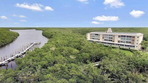 A riverside hotel with a dock, surrounded by dense greenery and a clear sky. - Beautiful 3/2 at Steven's Landing (Marco Island)