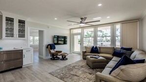 A modern living room with a sofa, a TV, a ceiling fan, and large windows.