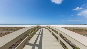 A wooden boardwalk leading to a beach with a clear sky.