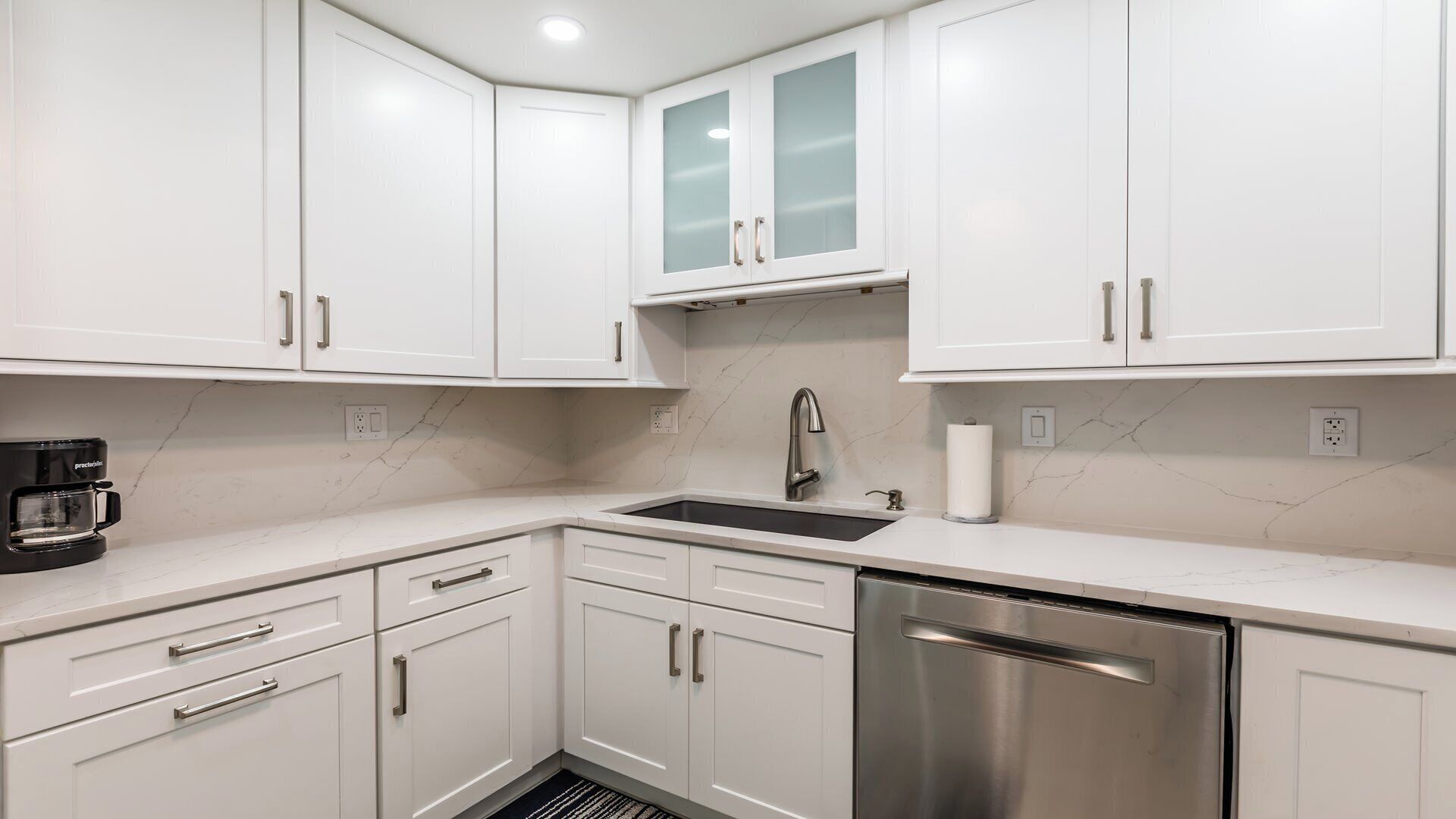 A modern kitchen with white cabinets, a stainless steel dishwasher, and a black coffee maker.
