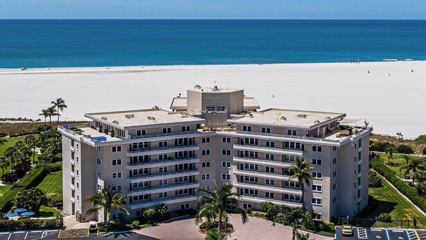 A multi-story hotel with a flat roof, located near a beach with a clear view of the ocean.