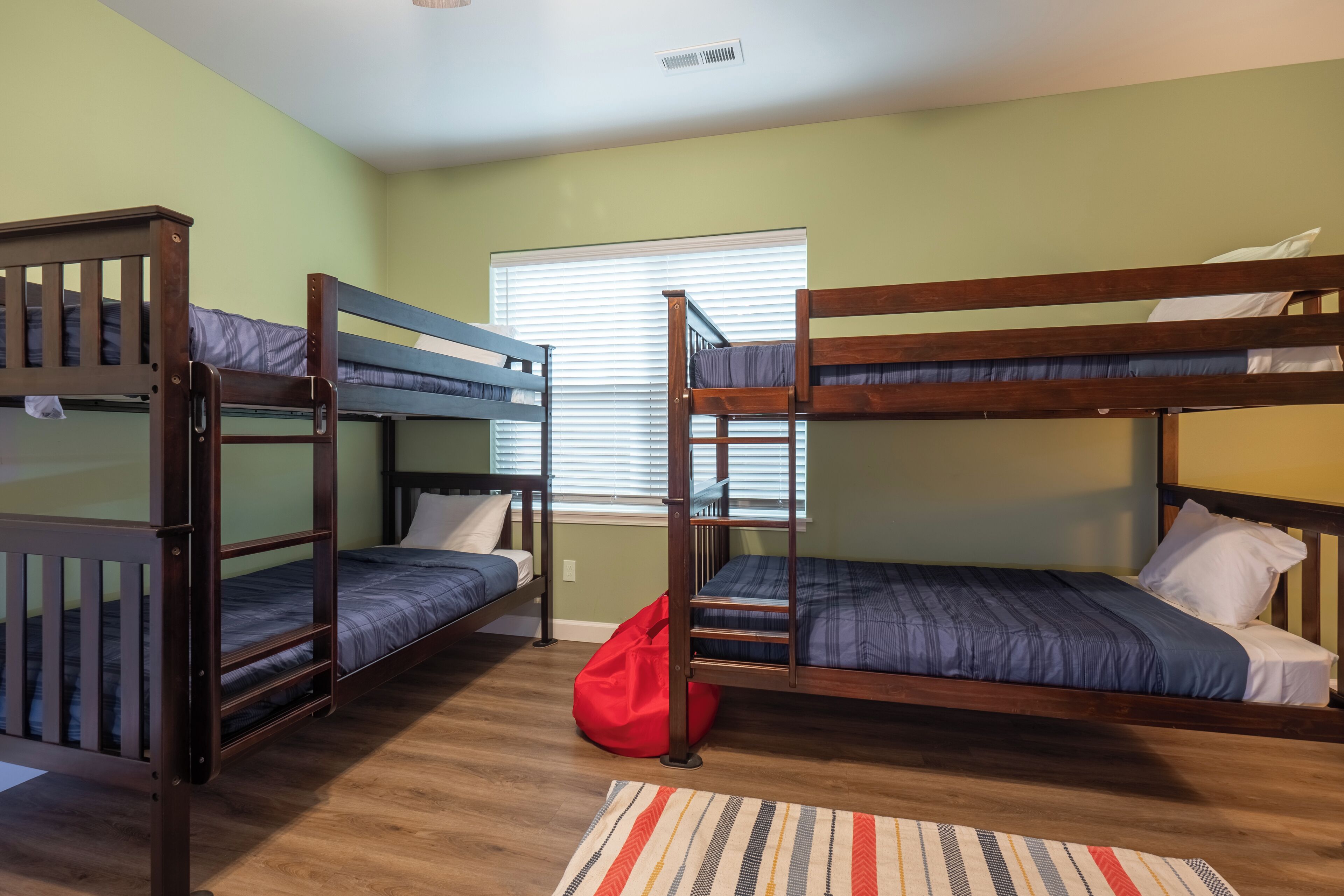 A dormitory room with bunk beds, a window with blinds, and a red bag on the floor.