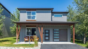 Une maison à deux étages avec un garage, une véranda couverte avec des chaises et un petit jardin.