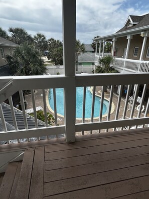 A wooden deck with a view of a swimming pool, palm trees, and a house in the background. - Flagler Beach Paradise (Flagler Beach)