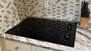 Eine Küche mit einem schwarzen Konvektionsbackofen, einem schwarzen Kochfeld und einer gefliesten Spritzschutzwand.