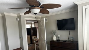 Ein Schlafzimmer mit Bett, Kommode, Fernseher und Deckenventilator.