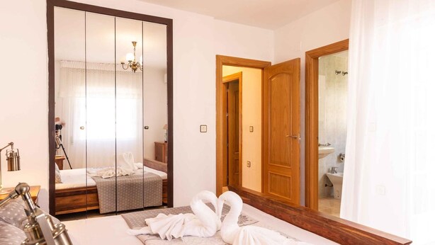 Ein Hotelzimmer mit einem großen Bett, einem Kleiderschrank, einem Spiegel, einer Nachttischlampe und einem durch eine geöffnete Tür einsehbaren Badezimmer.