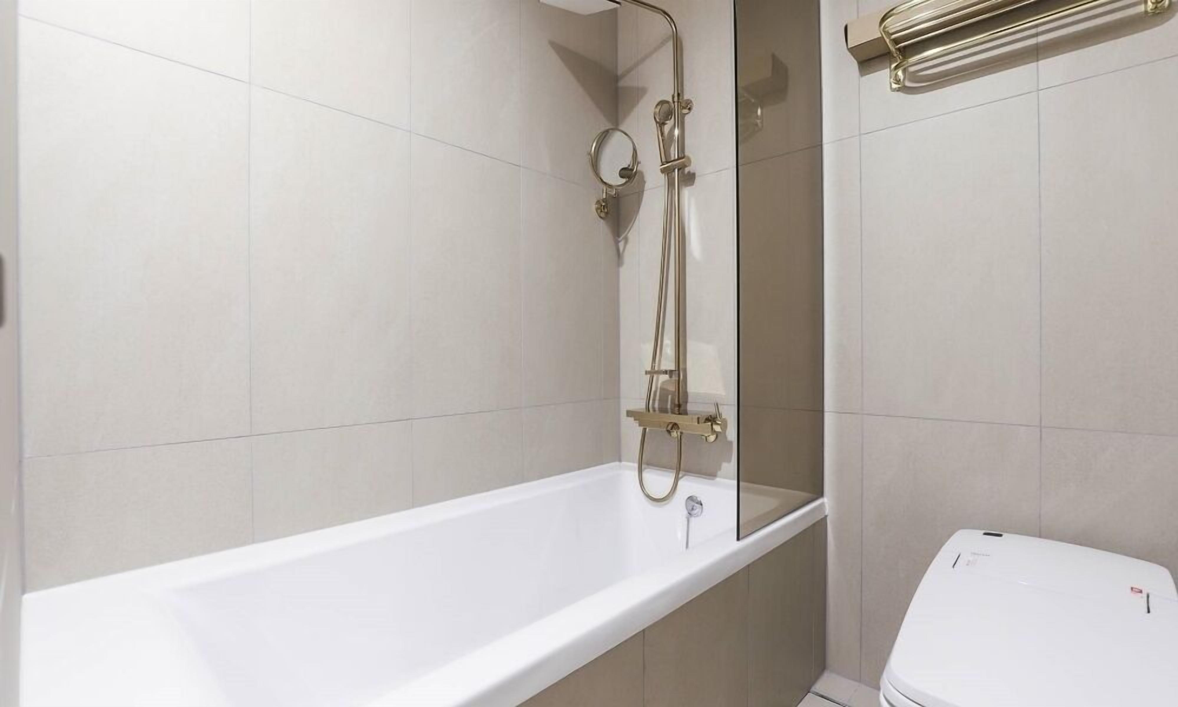 A modern bathroom with a white bathtub, a glass-enclosed shower, and a toilet.