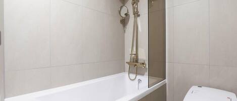 A modern bathroom with a white bathtub, a glass-enclosed shower, and a toilet.