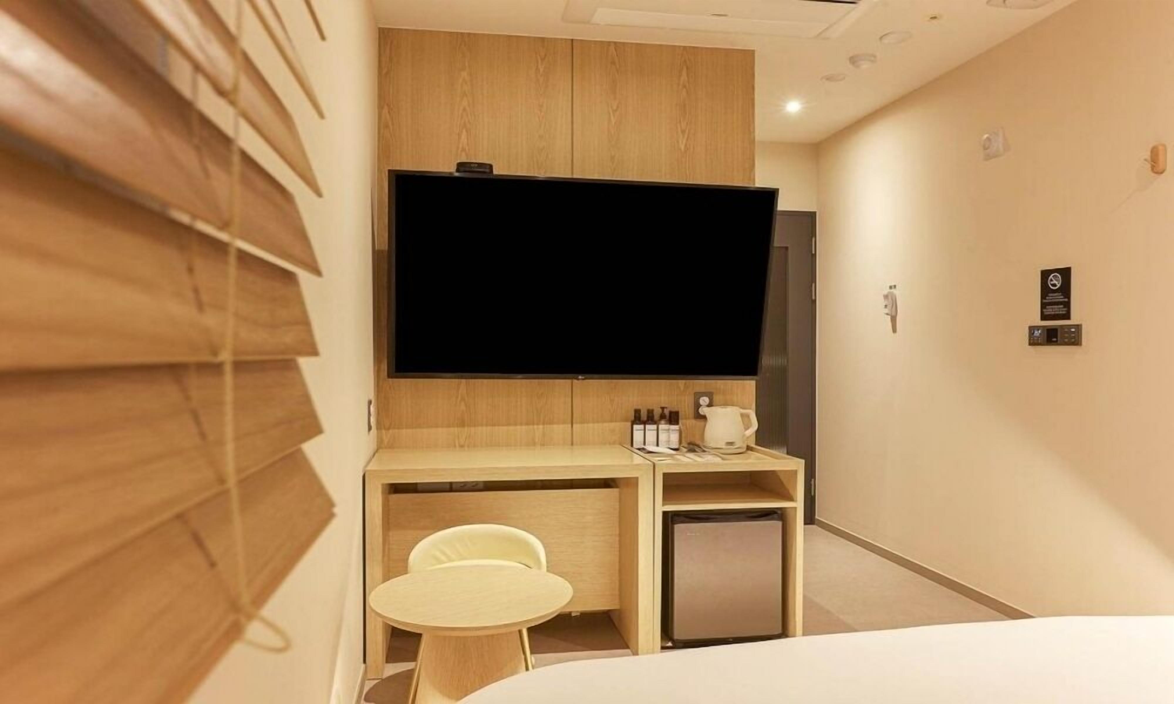 Habitación de hotel con cama, escritorio con silla, televisor y refrigerador pequeño.
