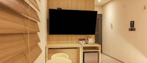 Habitación de hotel con cama, escritorio con silla, televisor y refrigerador pequeño.