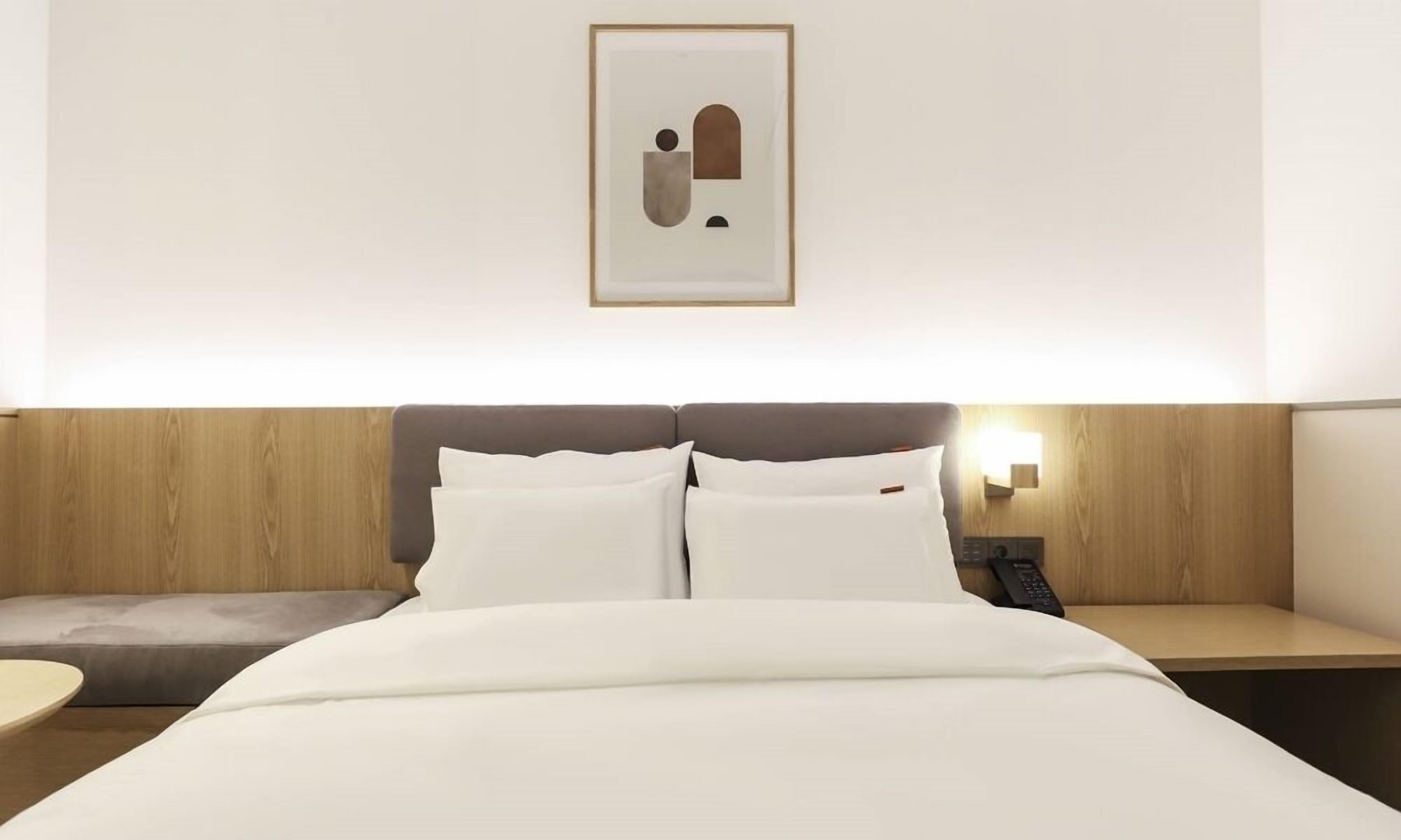A hotel room with a bed, bedside table, and a wall-mounted artwork.