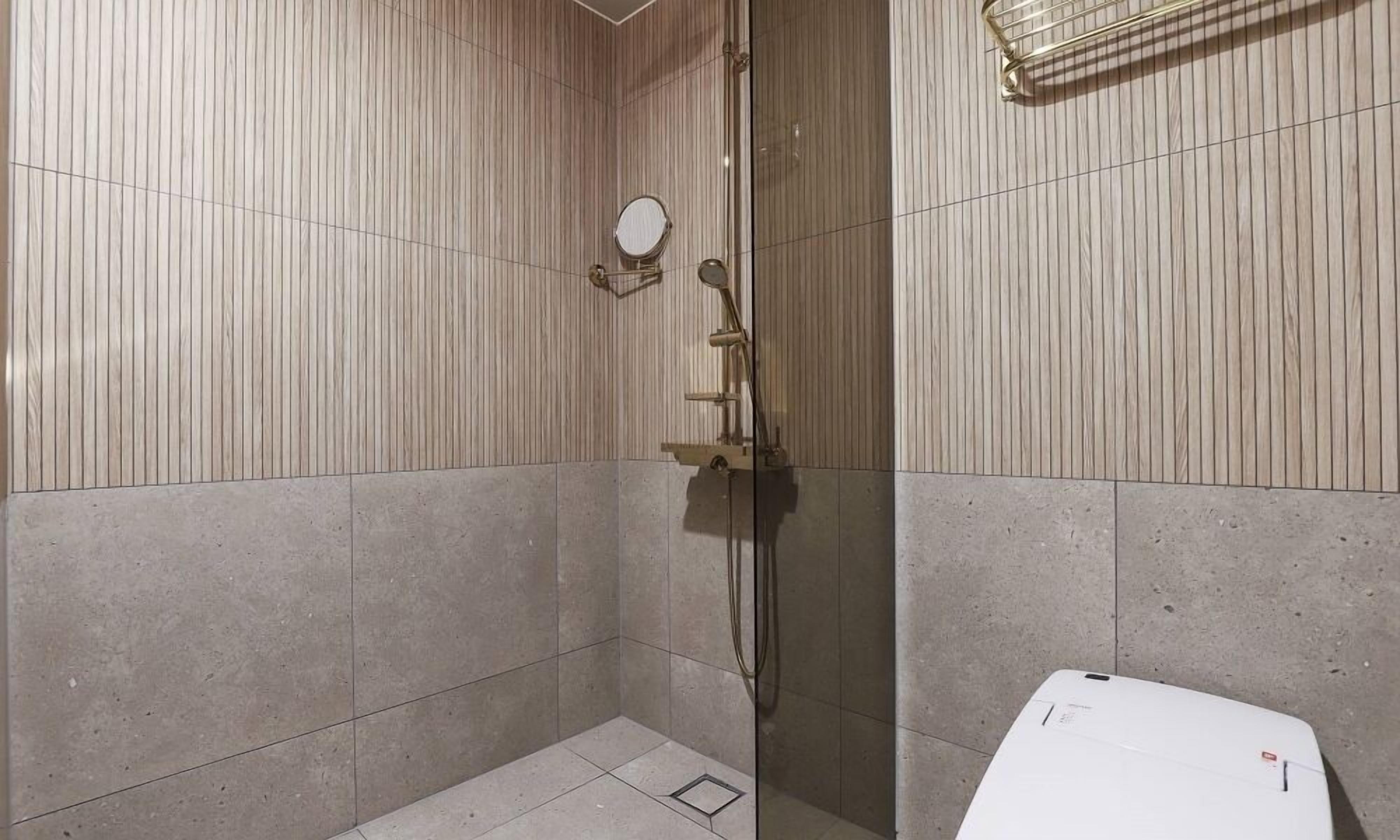 Um pequeno banheiro com azulejos, porta de vidro, chuveiro manual e espelho fixado na parede.