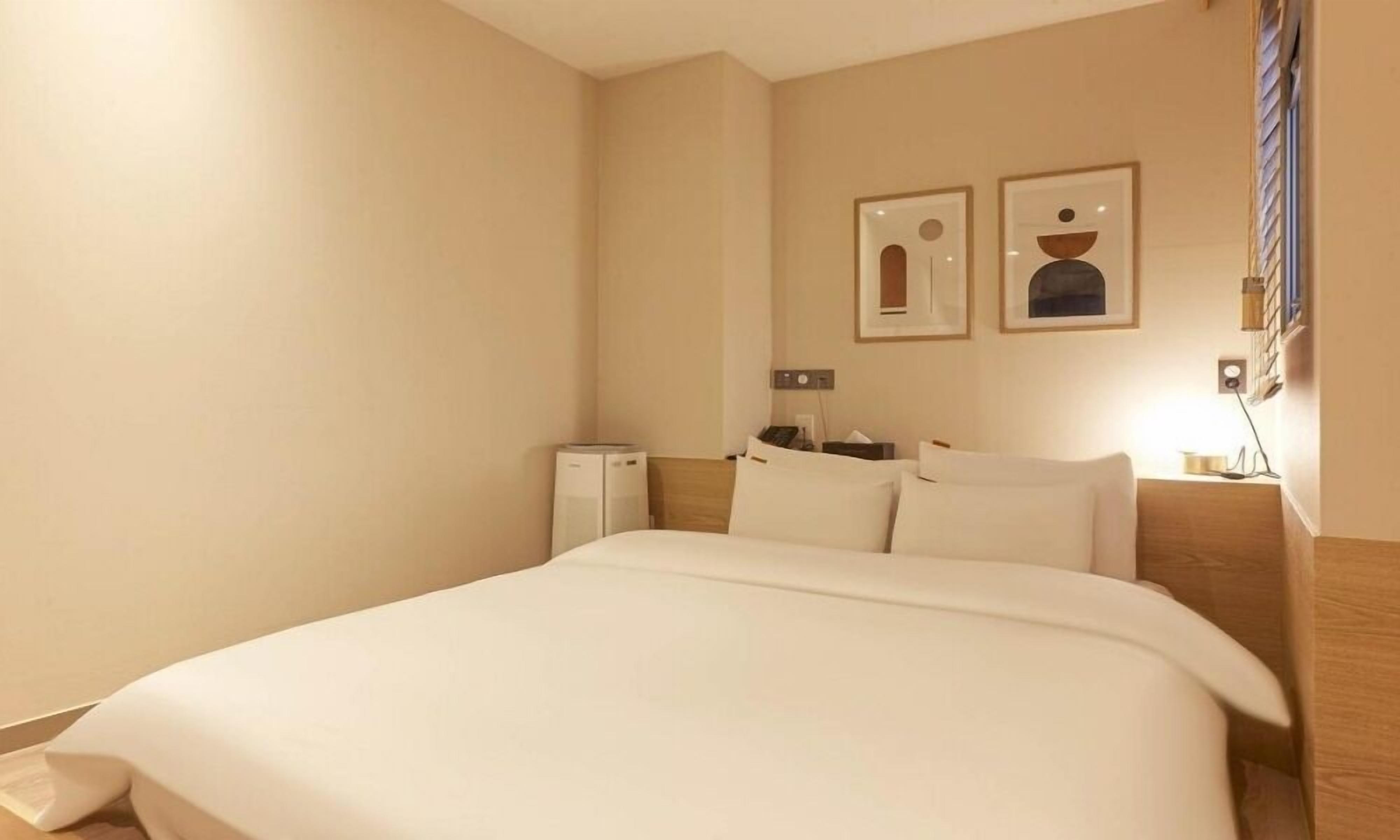 Hotelkamer met een groot bed, een bureau, een stoel, een klein tafeltje en twee ingelijste foto's aan de muur.