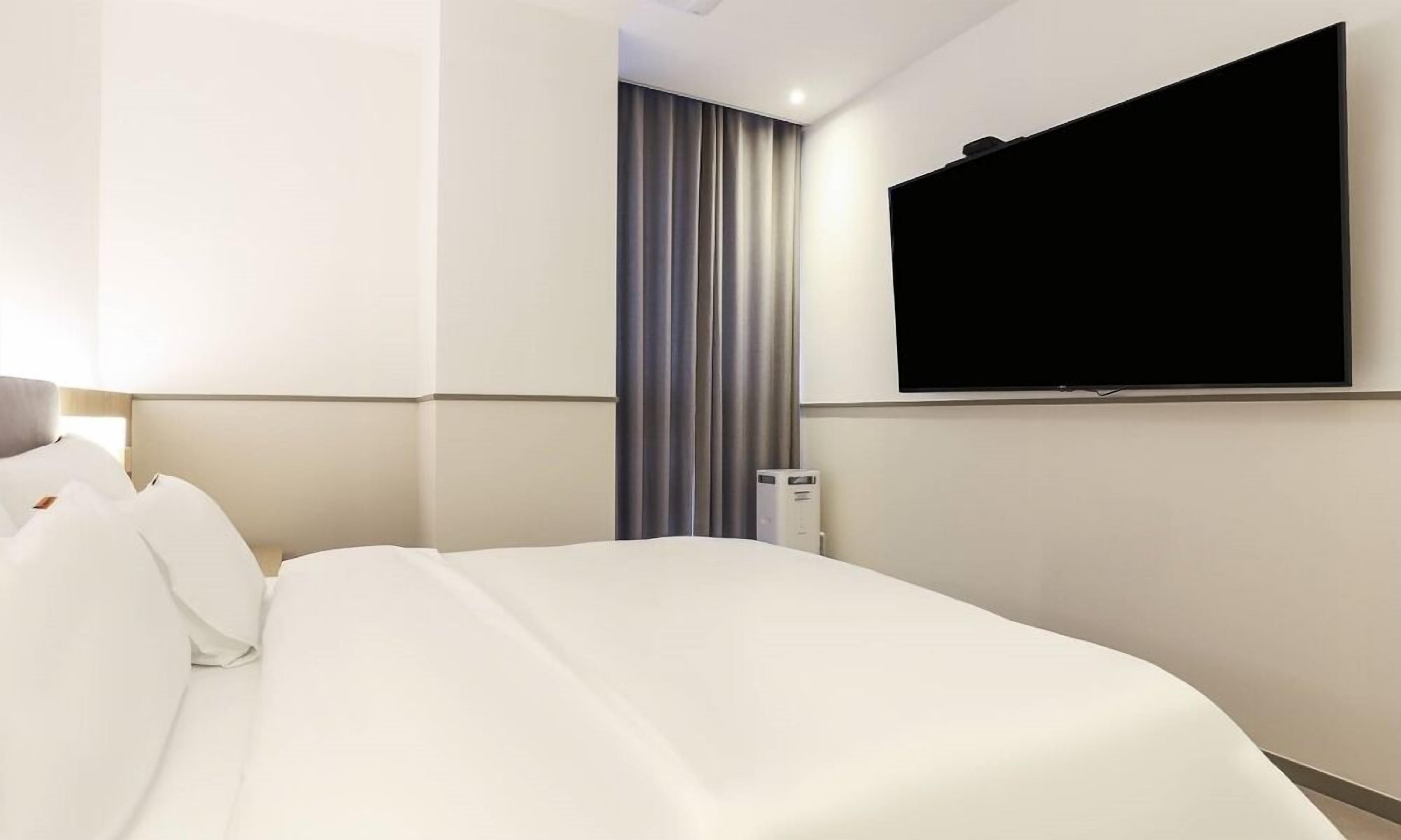A hotel room with a bed, a flat-screen TV mounted on the wall, and a thermostat on the wall.