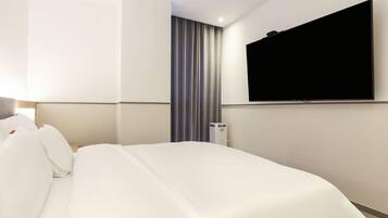A hotel room with a bed, a flat-screen TV mounted on the wall, and a thermostat on the wall.