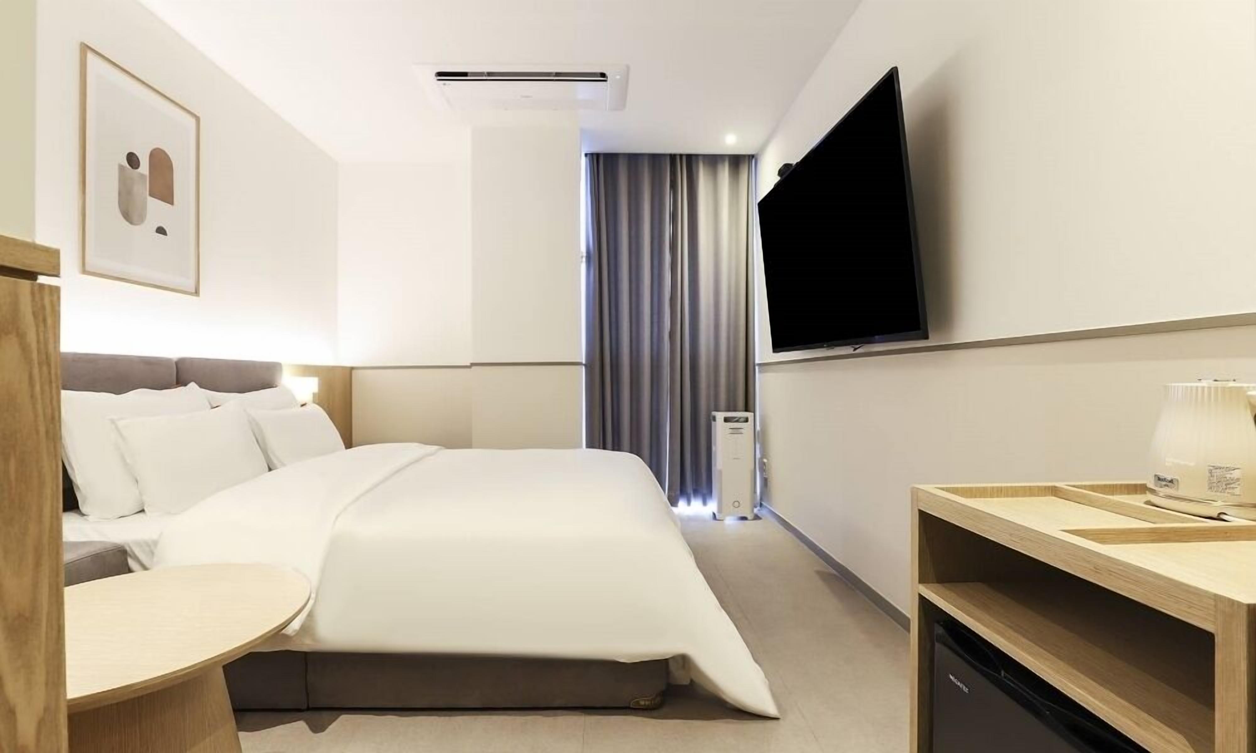 A hotel room with a bed, a TV, a desk, and a window with curtains.