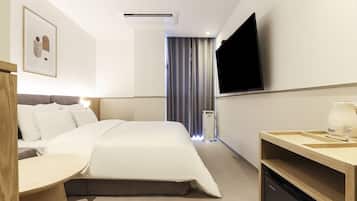 A hotel room with a bed, a TV, a desk, and a window with curtains.