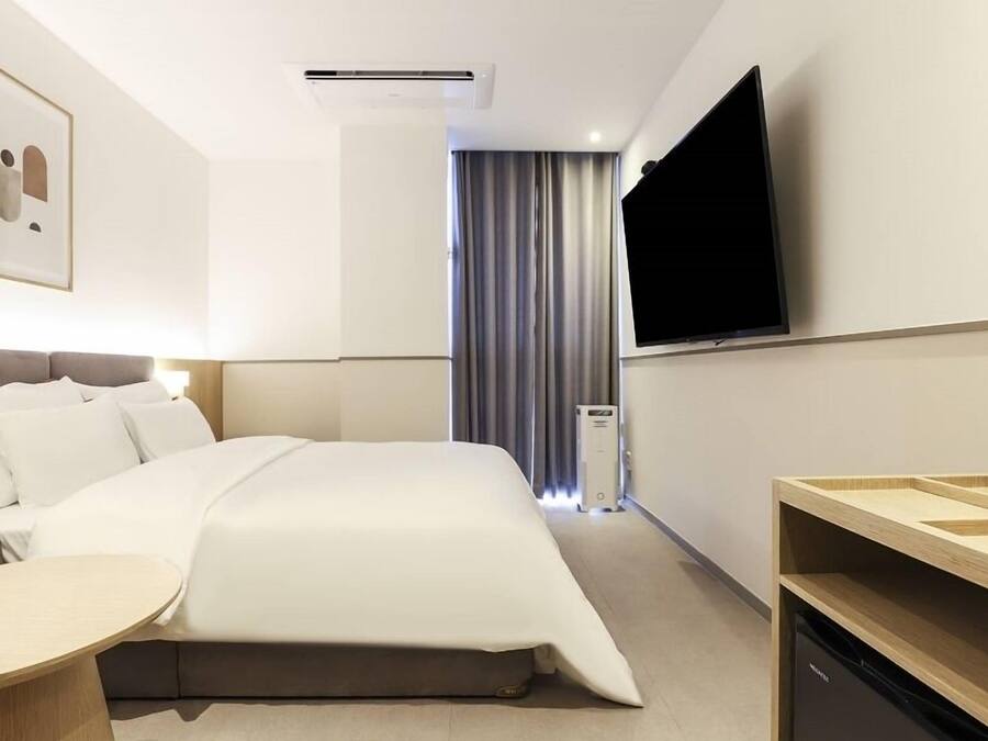 A hotel room with a bed, a TV, a desk, and a window with curtains.