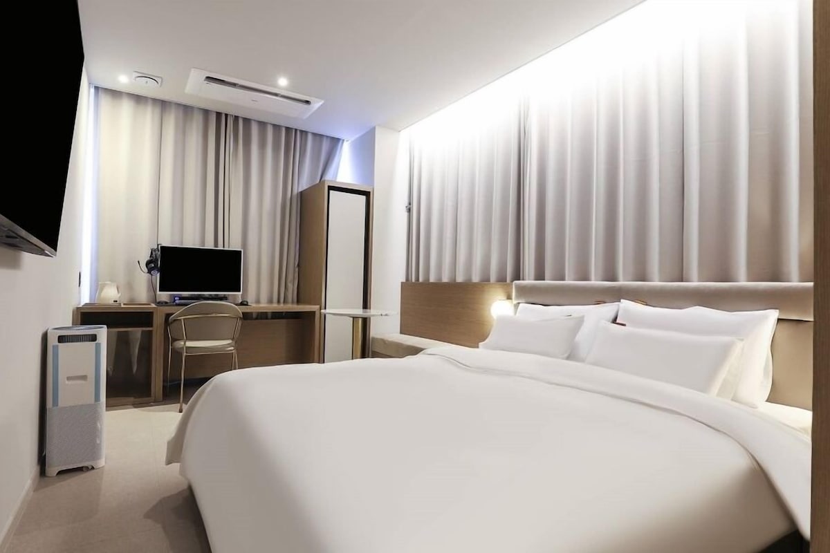 Habitación de hotel con una cama grande, un escritorio con computadora, televisor y aire acondicionado.