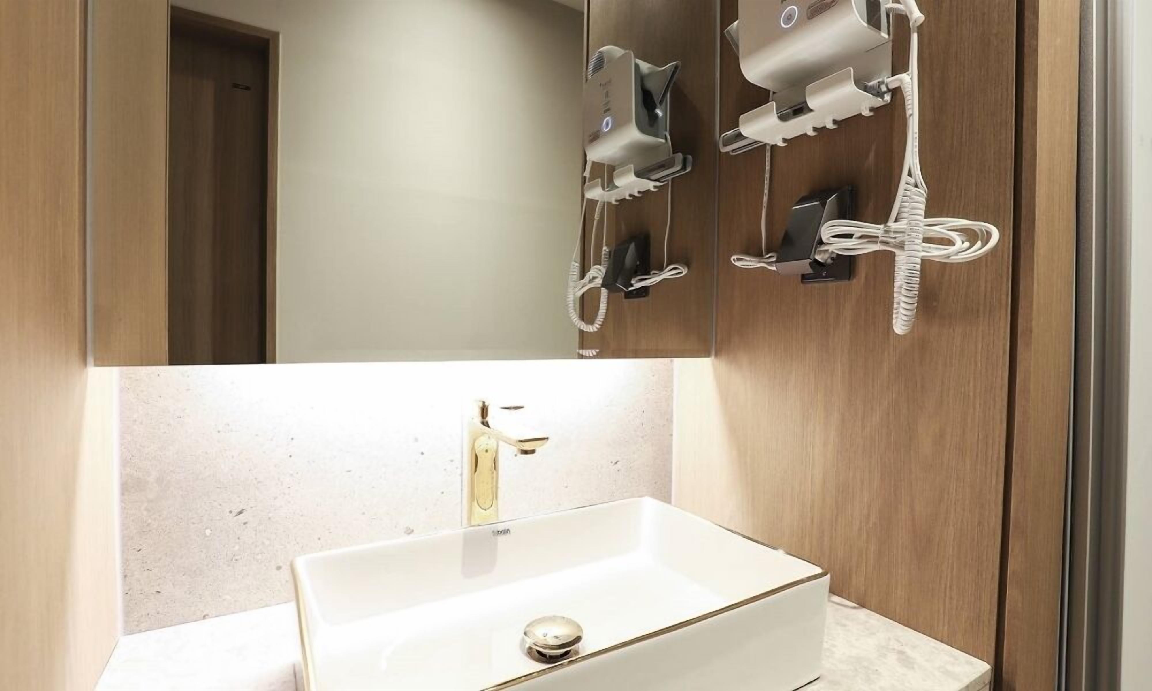 A bathroom with a white sink, a mirror, and two hair dryers mounted on the wall.