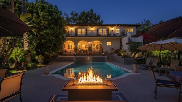 Una casa de dos pisos con piscina y una fogata al frente.